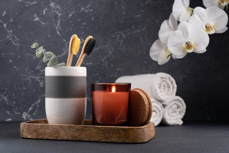 Eco friendly bathroom concept, sustainable lifestyle. Couple of bamboo toothbrush in a glass with white towels and orchid flowers on a wooden trayの写真素材