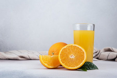Tasty fresh orange juice in glass with sliced orange and leaves on grey concrete backgroundの写真素材