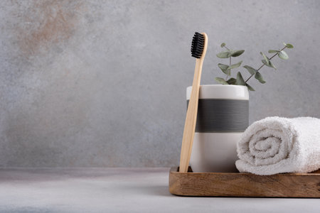 Eco friendly bathroom concept, sustainable lifestyle. Bamboo toothbrush in a glass with white towel and eucalyptus on wooden trayの写真素材