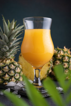 Pineapple juice in a glass with ice and fresh pineapple pieces on the dark backgroundの写真素材