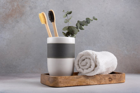 Eco friendly bathroom concept, sustainable lifestyle. Couple of bamboo toothbrush in a glass with white towel and eucalyptus on wooden trayの写真素材