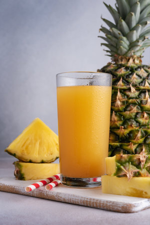 Pineapple juice in a glass with ice and fresh pineapple pieces on the grey backgroundの写真素材