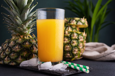 Pineapple juice in a glass with ice and fresh pineapple pieces on the dark backgroundの写真素材