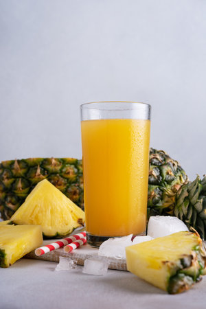 Pineapple juice in a glass with ice and fresh pineapple pieces on the grey backgroundの写真素材