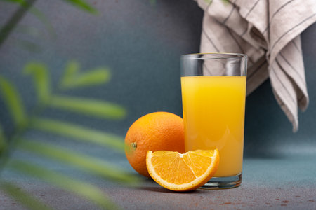 Tasty fresh orange juice in glass with sliced orange and leaves on dark grey concrete backgroundの写真素材