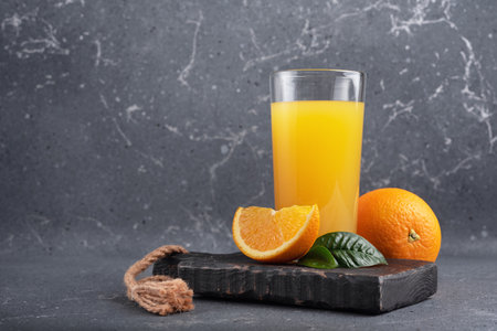 Tasty fresh orange juice in glass with sliced orange and leaves on dark grey concrete backgroundの写真素材