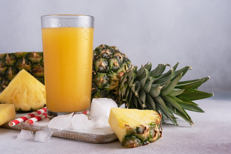 Pineapple juice in a glass with ice and fresh pineapple pieces on the grey backgroundの写真素材