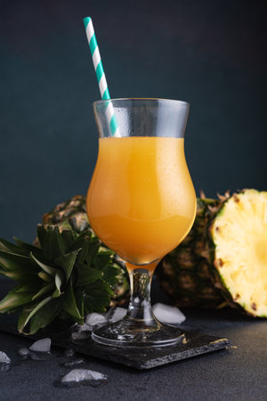 Pineapple juice or mocktail in a glass with ice and fresh pineapple pieces on the dark backgroundの写真素材