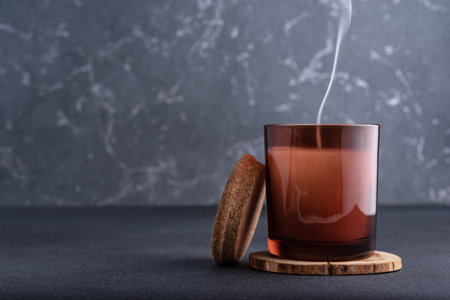 Cozy candle in brown glass jar with smoke on dark backgroundの写真素材