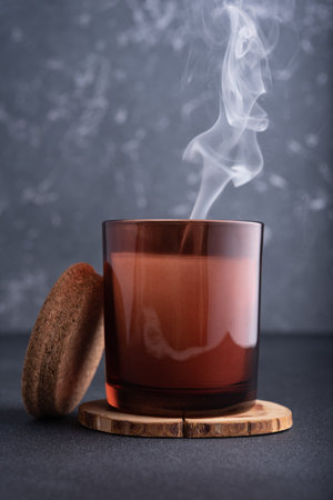 Cozy candle in brown glass jar with smoke on dark backgroundの写真素材