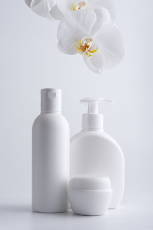 Group of white cosmetic bottles for template or mock-up with a white orchid on a gray backgroundの写真素材