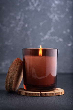 Cozy burning candle in brown glass jar on dark backgroundの写真素材