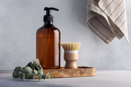 Eco friendly kitchen concept, sustainable lifestyle. Set for cleaning, as dish wash brush, dispenser bottle with eucalyptus on wooden trayの写真素材