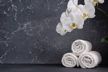 Dark background with white towels and orchid flowers for eco friendly, natural, beauty, salon, massage, shower or treatment product with copy spaceの写真素材