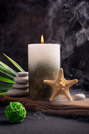 Golden candle with sea star, green leaves of plant and stones for relax, bath, spa, cozy interior on dark backgroundの写真素材