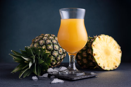 Pineapple juice or mocktail in a glass with ice and fresh pineapple pieces on the dark backgroundの写真素材
