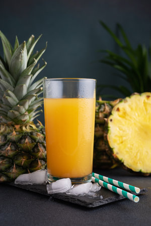 Pineapple juice in a glass with ice and fresh pineapple pieces on the dark backgroundの写真素材