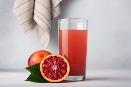 Red orange juice in glass with halved orange fruitsの写真素材