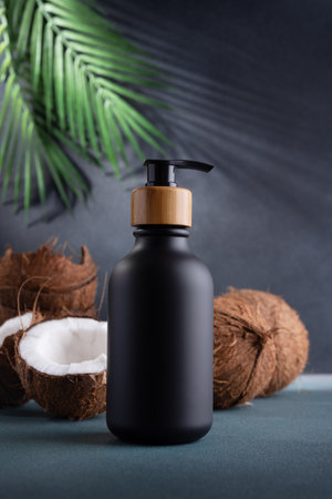 Black dispenser bottle and fresh coconut on dark background with palm leaves. Organic natural cosmetics with coconut oil. Plastic packaging products for branding, mock up.の写真素材