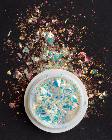 Glitter for manicure and nail art. Multicolored shimmer in white jar on black background.の写真素材