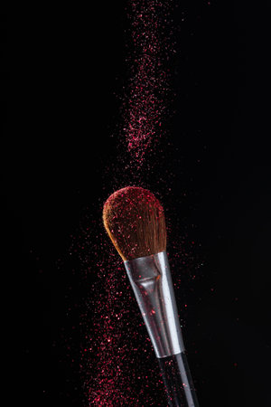Red glitter falls on make-up brush in black background. Luxury make-up concept.の写真素材