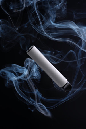 White electronic cigarette or vape on a black background with smoke. The concept of modern smoking, vaping and nicotine.の写真素材