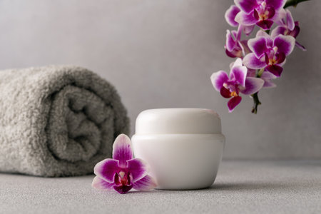 White cosmetic cream jar, product mockup on gray background with orchid flower and towel. Face cream moisturizer showcase, natural organic luxury skincare spa cosmetics.の写真素材