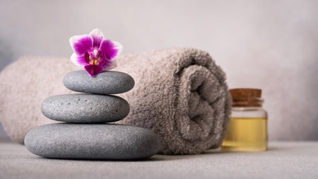 Spa still life with smooth pebbles, a rolled gray towel, and a vibrant purple orchid. The composition exudes tranquility and balance, perfect for wellness and relaxation themes.の写真素材