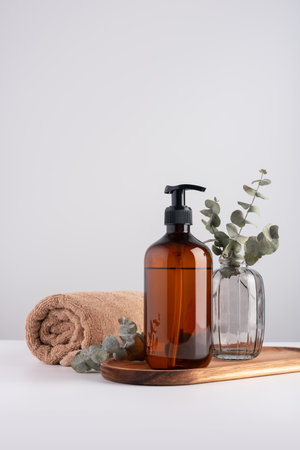 Bath and wellness still life with terry cotton towel and cosmetic bottle for healthy wellbeing. Brown transparent dispenser bottle, cotton towel and eucalyptus.の写真素材