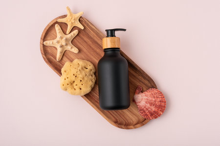 Black dispenser bottle with starfish, seashells and natural sea sponge on wooden tray for organic cosmetic mock up.の写真素材