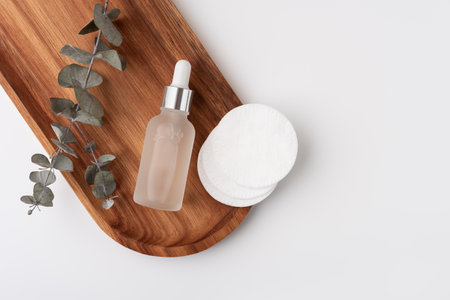 Glass dropper bottle with transparent liquid essence, serum or cream on wooden tray with cotton pads. Natural cosmetic concept.の写真素材