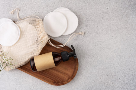 Flat lay featuring eco-friendly skincare essentials, including reusable cotton pads in a drawstring bag, a brown glass pump bottle, and a wooden tray. Perfect for sustainable beauty enthusiasts. Zero-waste and plastic-free skincare routines with reusable and natural materials.の写真素材