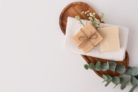 Folded soft white terry towel with soap bar on a wooden tray, top view. Clean bathroom or spa concept.の写真素材