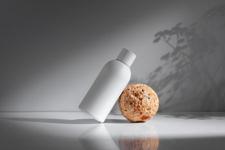 Minimalist white bottle on a light grey background with shadows of plant leaves, representing beauty, wellness, or skincare product packaging.の写真素材