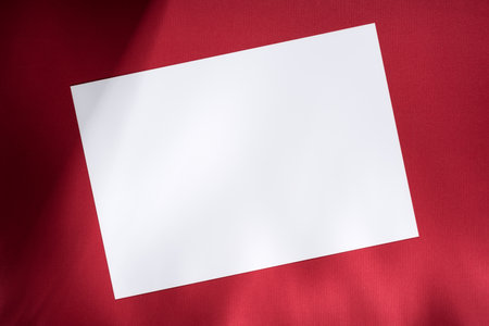 Blank white paper on red background with soft shadows, perfect for mockup, template, or design presentation. Clean minimalist concept with contrast and elegant simplicity.の写真素材