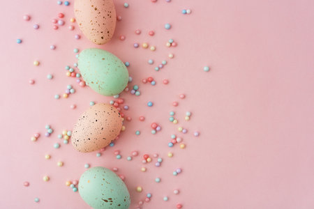 Four Easter eggs in pastel pink and green colors are artistically placed on a pink surface, surrounded by an array of small, colorful candy decorations, creating a festive atmosphere.の写真素材