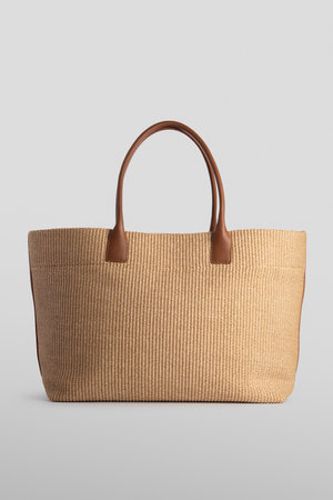 Natural raffia tote bag on white background. Minimalist, eco-friendly accessory with woven texture. Perfect for summer, casual wear, or sustainable fashion design presentations.の写真素材