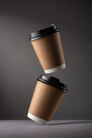 Flying disposable coffee cups on dark background. Minimalist style with motion and balance concept. Paper takeaway cups with black lids for hot drinks.の写真素材