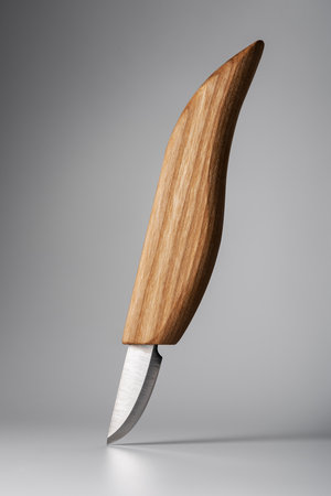 Minimalist wood carving knife standing upright on grey background. Modern handcrafted object with elegant design, clean lines, and sharp steel blade. Studio lighting emphasizes shape and texture.の写真素材