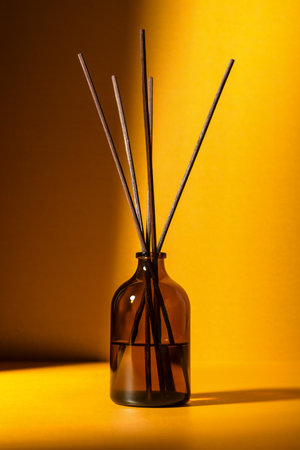 Amber glass diffuser bottle with fragrance sticks against a warm golden background. Minimal wellness and aromatherapy concept with soft lighting and shadows.の写真素材