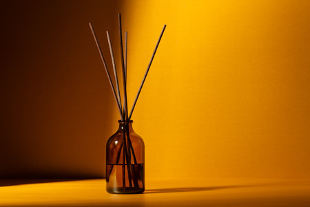 Amber glass diffuser bottle with fragrance sticks against a warm golden background. Minimal wellness...