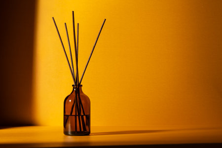 Amber glass diffuser bottle with fragrance sticks against a warm golden background. Minimal wellness and aromatherapy concept with soft lighting and shadows.の写真素材