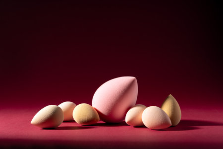 Cosmetic sponges arranged on a red background with dramatic lighting. Beauty blenders in various shades create a stylish and elegant composition for skincare or makeup visuals.の写真素材
