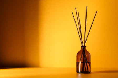 Amber glass diffuser bottle with fragrance sticks against a warm golden background. Minimal wellness and aromatherapy concept with soft lighting and shadows.の写真素材