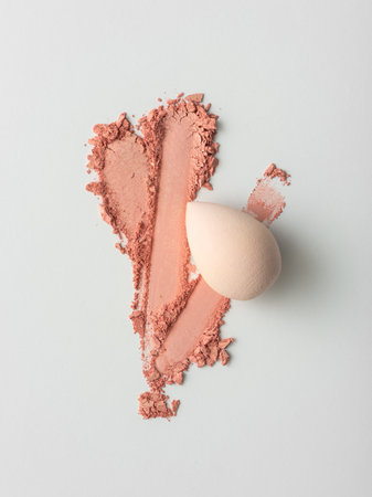 Crushed pink blush powder smear and blending sponge on white background. Close-up of cosmetic texture for beauty or skincare design. Soft and elegant makeup concept.の写真素材