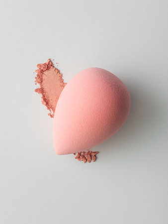 Makeup sponge with smear of blush powder on a light background. Colorful beauty tools arranged in minimal, modern style for cosmetics or skincare product concept.の写真素材