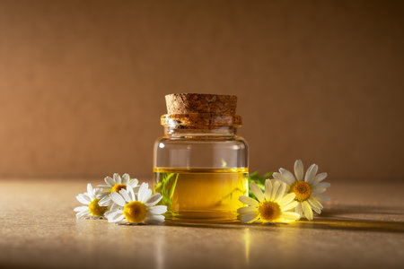 Glass bottle with cork filled with chamomile essential oil, surrounded by fresh chamomile flowers. Natural skincare, wellness and aromatherapy concept in warm, soft lighting.の写真素材