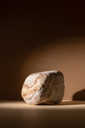 Stone podium on a neutral brown background with soft shadows. Minimal natural display setup for...