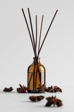 Brown glass reed diffuser with aromatic sticks and star anise spices on light background. Concept of fragrance, home decor, wellness, spa, relaxation and natural lifestyle.の写真素材