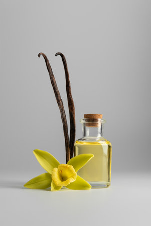 Glass bottle with vanilla essential oil, vanilla flower, and pods on light background. Natural cosmetic essence concept symbolizing purity, relaxation, and elegance.の写真素材